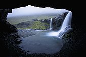 waterfalls over a rock ledge as viewed from inside a cave; iceland