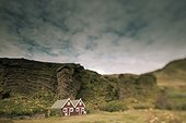 a red house with a peaked roof beside a rock ledge; iceland