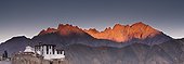 a building on a rock ledge with alpenglow over the mountains in the background; lamayuru ladakh india