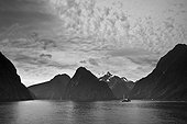 a boat in the water along the coast surrounded by mountains; milford sound south island new zealand
