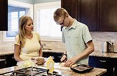 Young man prepares lunch in the kitchen at home as his mother looks on and provides support; Edmonton, Alberta, Canada
