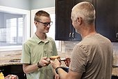 Young man serving his dad a sandwich in the kitchen at home; Edmonton, Alberta, Canada