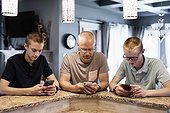 Father and two sons sit at the kitchen island at home using their smart phones; Edmonton, Alberta, Canada
