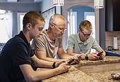 Father and two sons sit at the kitchen island at home using their smart phones; Edmonton, Alberta, Canada