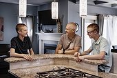 Father and two sons sit at the kitchen island at home talking together; Edmonton, Alberta, Canada