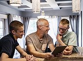 Father and two sons sit at the kitchen island at home using a tablet and talking together; Edmonton, Alberta, Canada