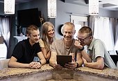 Parents and two sons sit at the kitchen island at home using a tablet and viewing content together; Edmonton, Alberta, Canada