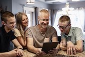 Parents and two sons sit at the kitchen island at home using a tablet and viewing content together; Edmonton, Alberta, Canada