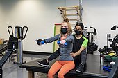A paraplegic woman doing bilateral raises during her workout with her trainer: Edmonton, Alberta, Canada