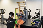 A paraplegic woman doing bilateral raises during her workout with her trainer; Edmonton, Alberta, Canada