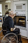 Man with double limb amputations using the oven in the kitchen at home; St. Albert, Alberta, Canada