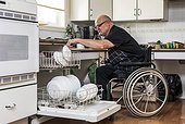 Man with double limb amputations loading the dishwasher in the kitchen at home; St. Albert, Alberta, Canada