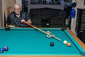 Man with double limb amputations playing a game of pool at home; St. Albert, Alberta, Canada