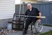 Man with double limb amputations doing yard work in his backyard with a broom; St. Albert, Alberta, Canada