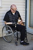 Man with double limb amputations sitting outside his house with his pet cat on his lap; St. Albert, Alberta, Canada