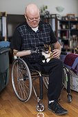 Man with double limb amputations sitting in his house with his pet in his lap; St. Albert, Alberta, Canada