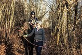 A young girl with Cerebral Palsy and her trainer working with a horse on a trail ride during a Hippotherapy session; Westlock, Alberta, Canada