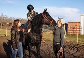 A young girl with Cerebral Palsy, her Mom and her trainer working with a horse during a Hippotherapy session; Westlock, Alberta, Canada