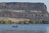 A bass angler fishes in The Devils Punchbowl on Banks Lake below the towering north end of Steamboat Rock, Steamboat Rock State Park; Grand Coulee, Washington, United States of America