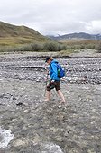 Mature female hiker crossing a stream barefoot in the Marsh Fork of the Canning River valley in the Brooks Range, Arctic National Wildlife Refuge, Alaska, Summer