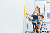 Couple In Casual Plaid Shirts Paint House Wall Together. Diy Renovation Concept