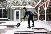 Man In A Hat And Leather Jacket Clearing Snowy Floor With A Plastic Shovel
