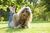 UK, London, Young woman lying in park and using mobile phone