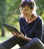 UK, London, Young woman sitting in park and using digital tablet