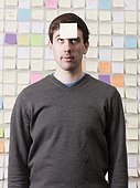Studio shot of young man looking at post-it note on forehead