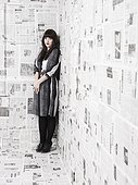 Studio Shot of a young woman standing in the corner of a room covered with newspaper