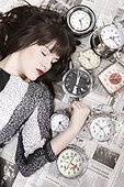 Studio shot of young woman sleeping with alarm clocks