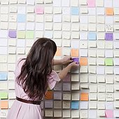Studio shot of young woman putting sticky notes on wall covered in adhesive notes