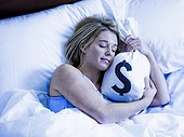 Young woman sleeping in bed with money bags