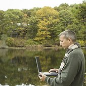 Side profile of a mature man using a laptop at a lakeside