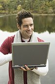 Mature man using a laptop at lakeside and smiling