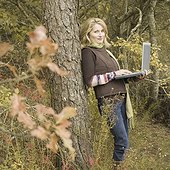 Mature woman leaning against a tree and using a laptop