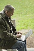 Side profile of a mature man sitting in a lawn and using a laptop