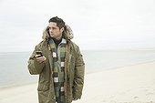Mature man holding a mobile phone on the beach