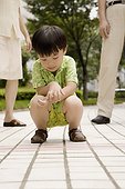 Boy crouching on a footpath with his grandparents standing behind him