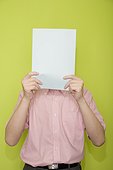 Male office worker hiding his face with a paper