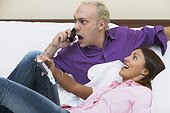 Young man using a mobile phone on the bed with a young woman leaning on him
