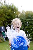 Blond girl with spalshing with water in garden