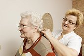 Geriatric nurse putting on necklace for old woman