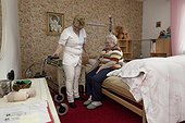 Geriatric nurse helping old woman in bed with walking frame