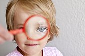 Blond girl looking through magnifying glass, close-up