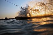 A wakeboarder sprays water in front of the setting sun at a wakeboard cable park in Cresson, Texas.