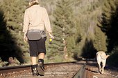 A woman and her dog walk along some train tracks to their next fishing spot.