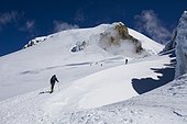 Skiers skin up a snowy ridge at sunrise on a blue bird day.