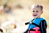 A 3 year old boy stands in a life jacket on the shores of Bear Lake, Utah.
