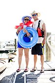 A woman stands with inner tubes and her son next to wooden kayaks at the Bear Lake Marina.